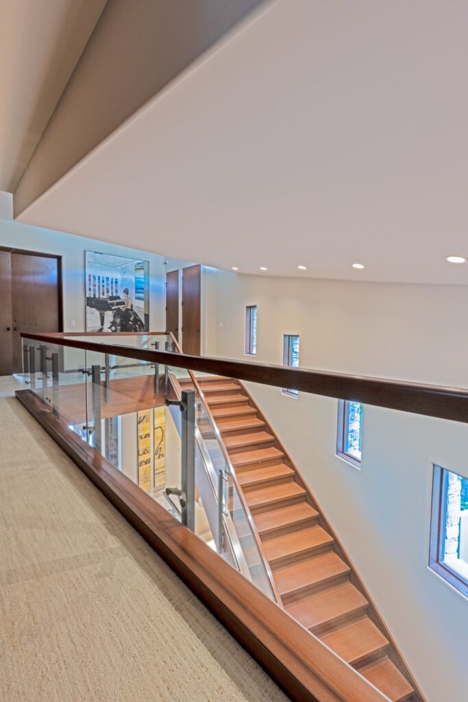 Photo of a short glass wall with wood railing that descends into a glass stair railing