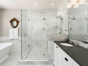 Frameless glass shower doors shown in a stylish bathroom with marble and black granite counter tops.