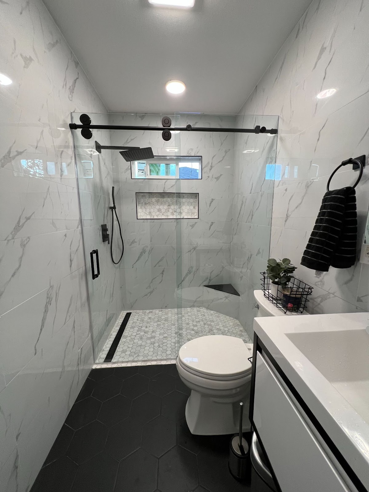 The photo features "Barn Door" style glass shower doors in a bathroom with marble walls and black tile floor