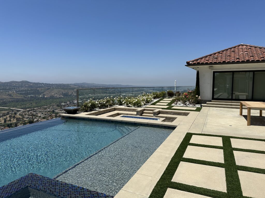 Photo of a large custom home on a hillside in Orange County with custom glass railings in their outdoor space next to an infinity pool